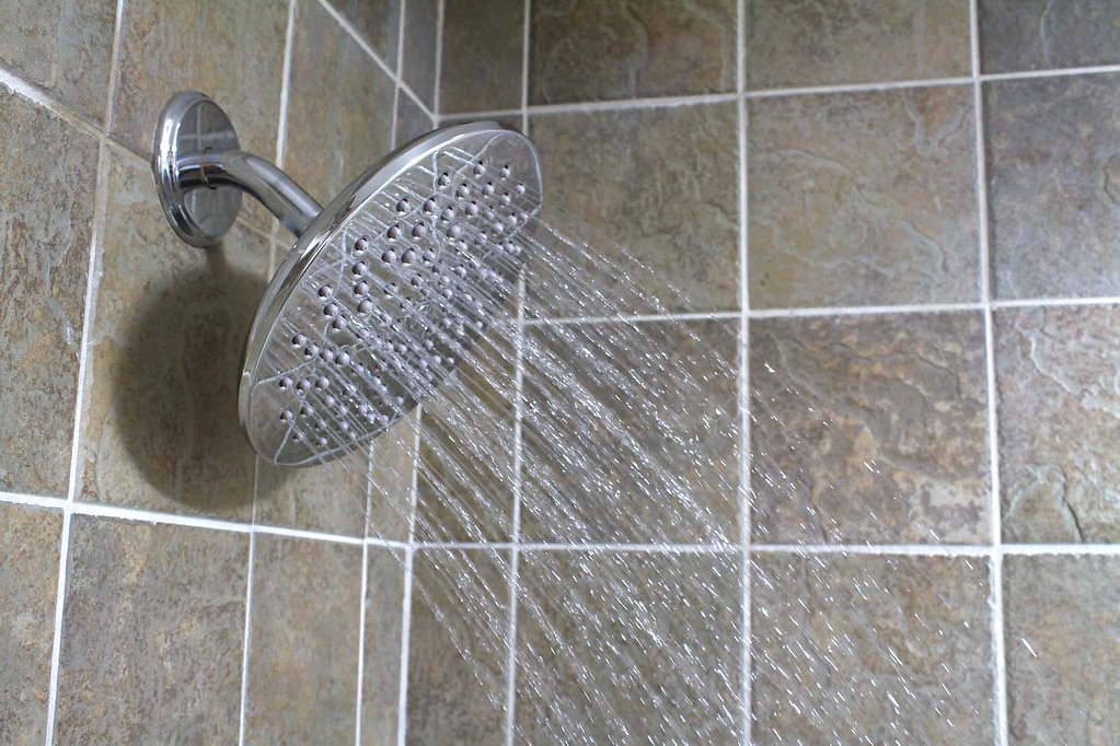 Alcachofa de ducha cromada con agua cayendo sobre azulejos de baño